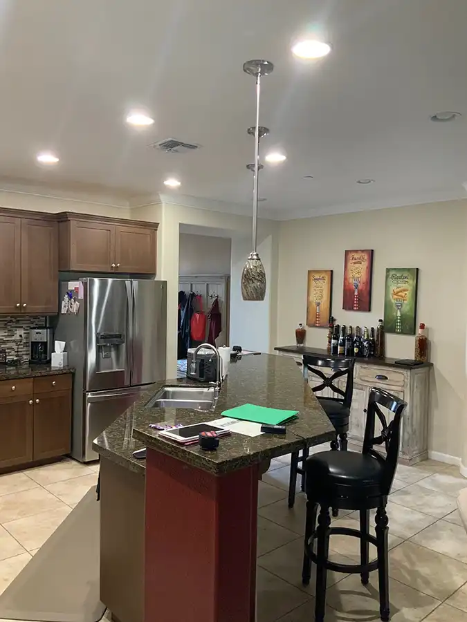 White wood cabinets with brass fixtures, black and white geometric tile flooring, stainless steel appliances with cobalt blue gas stove/oven. Island in center with pot rack above