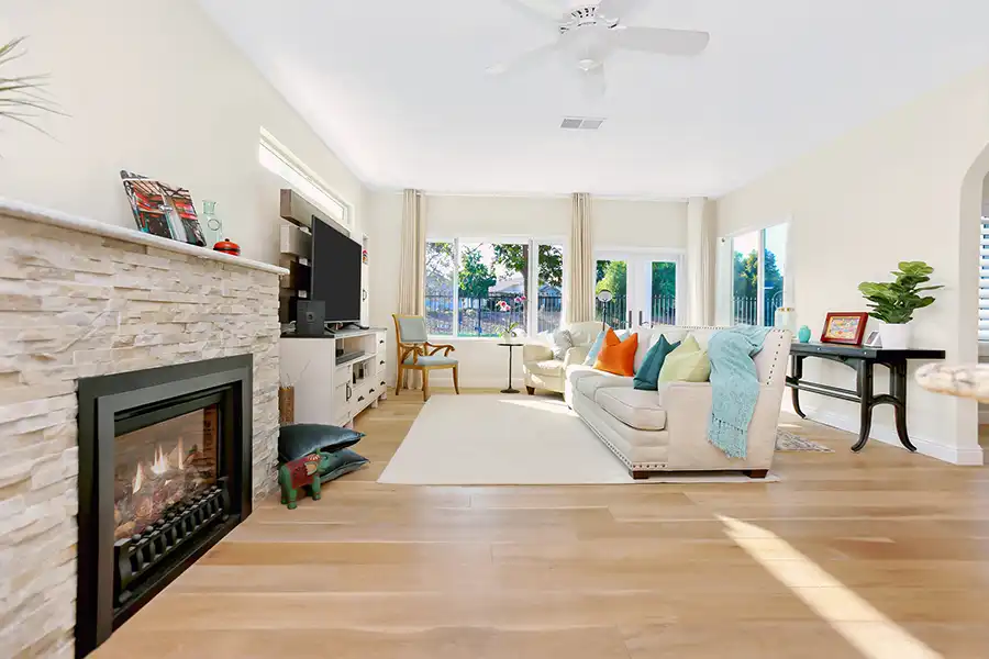 Light hardwood flooring, white cabinet, matte black fireplace insert surrounded by rough stone mantel. White couch and area rug with some colorful pillows