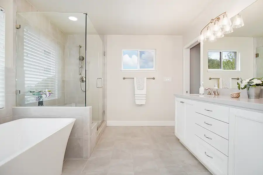 White cabinet, white stone countertop, stone tile flooring, brushed nickel fixtures, glass enclosed shower, white standing tup.