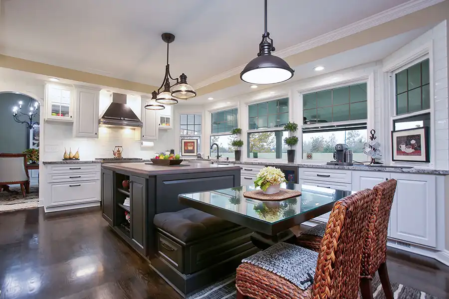 Dark hardwood flooring, white cabinets, matte black hardware and fixtures, stainless steel hood, gas range, dark gray island with banquette, small glass top dining table, coffered ceilings