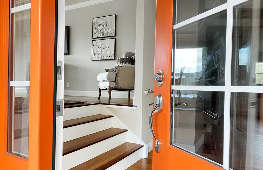 Orange door opens to a foyer with stairs leading into a house