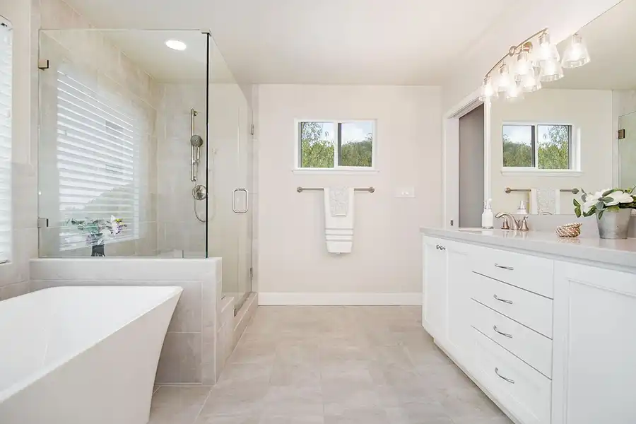 White bathroom with stone floor and clear glass shower and white geometric tub