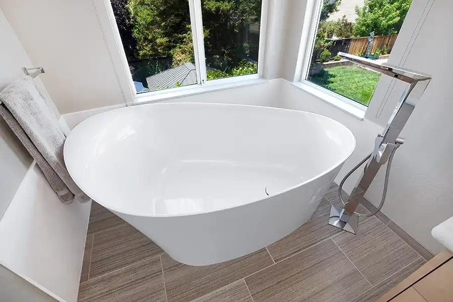 013_5558_Arlene_way7 Creamy almond walls, light-toned wood cabinets with modern hardware, light colored stone countertops with twin sinks, a soaking tub in the corner by a window, with a glass-surround shower in the opposing corner, and wood motif tile on the floors.