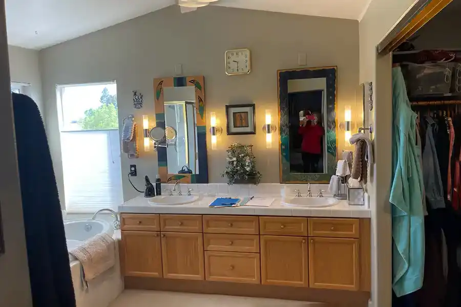 02 BEFORE ARLENE IMG_0345 taupe walls, medium-toned wood cabinets, white tile countertops with twin sinks, soaking tub in corner by window, with shower in opposing corner.