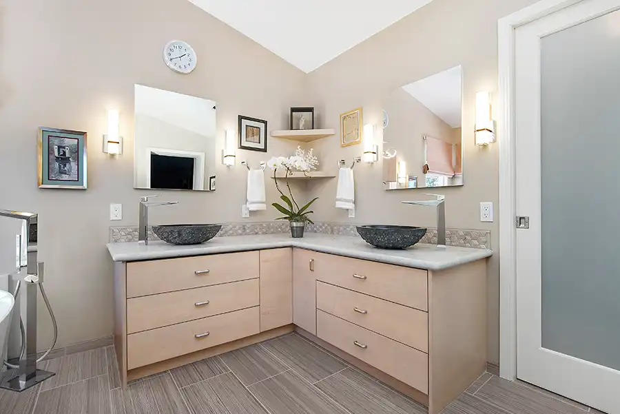 02_5558_Arlene_way2 Creamy almond walls, light-toned wood cabinets with modern hardware, light colored stone countertops with twin sinks, a soaking tub in the corner by a window, with a glass-surround shower in the opposing corner, and wood motif tile on the floors.