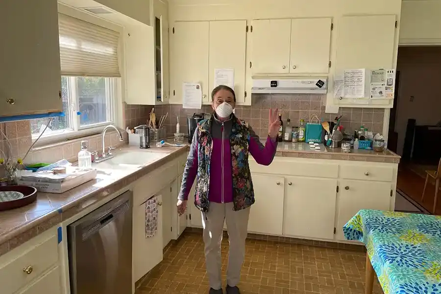 White wood cabinets with brass fixtures, black and white geometric tile flooring, stainless steel appliances with cobalt blue gas stove/oven. Island in center with pot rack above