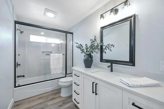 Brentwood hall bath with a black-framed glass tub enclosure, recessed niche, white Shaker vanity, and black Moen Genta faucet.