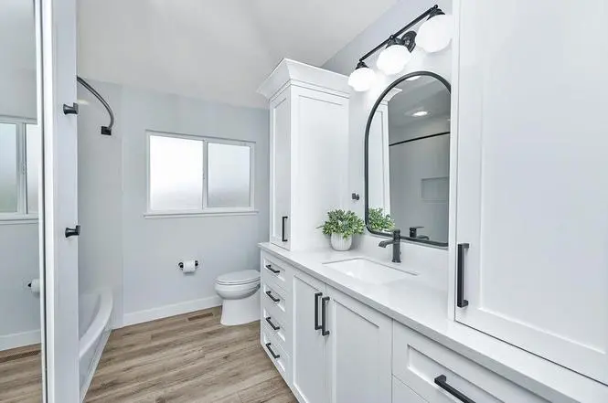 Bedroom bath with white Shaker vanity towers beside an arched black mirror, globe vanity light, and black Moen Genta faucet.