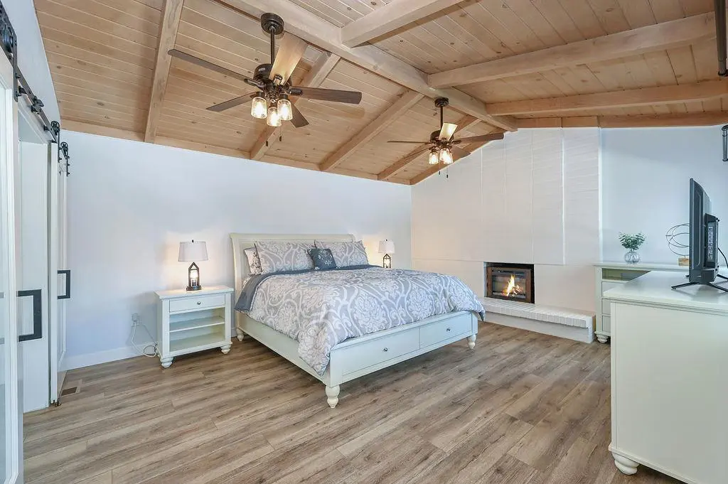 Primary bedroom in a 1961 Brentwood home, keeping the original wood ceiling, exposed beams, and fireplace from the former living room.