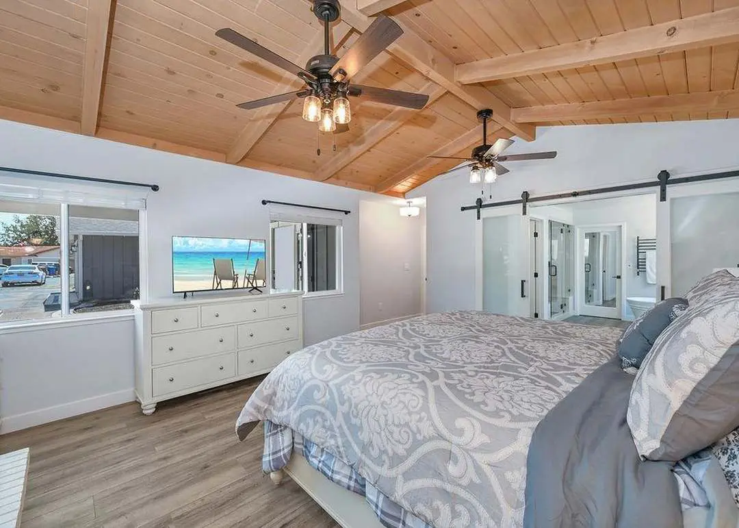 Primary bedroom under a beamed wood ceiling, with satin-glass barn doors open to the new primary bath and steam shower.
