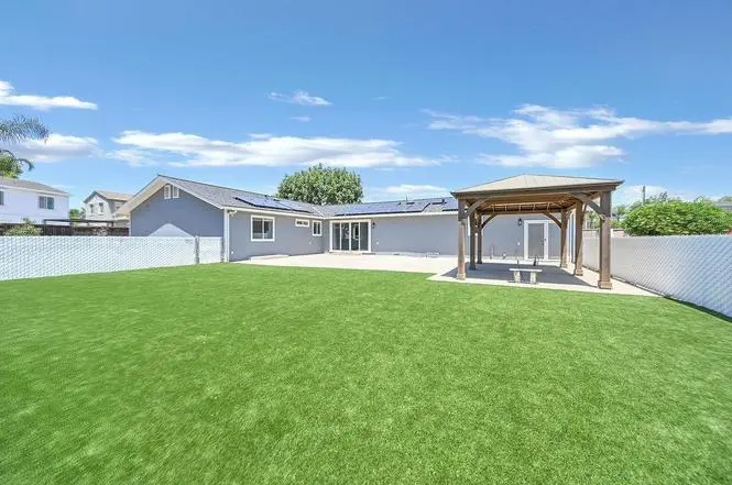 Back of the Brentwood home with an expanded broom-finished concrete patio, four-panel sliding door, wood gazebo, and green lawn.
