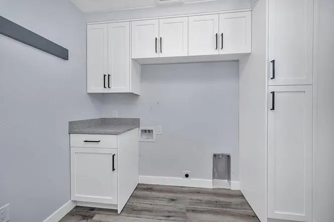 Laundry room with custom white Shaker cabinetry, tall storage cabinets, and a Piedrafina Pebble Beach countertop beside the washer space.