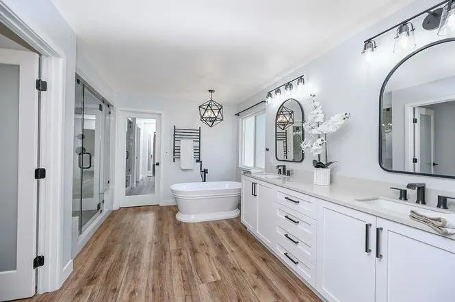 Primary bath with freestanding Versailles tub, glass steam shower, black heated towel warmer, and double vanity with arched mirrors.