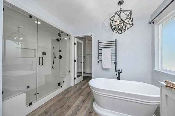 Enclosed steam shower with built-in bench and Delta Trinsic fixtures beside a freestanding tub and Amba Radiant heated towel warmer.