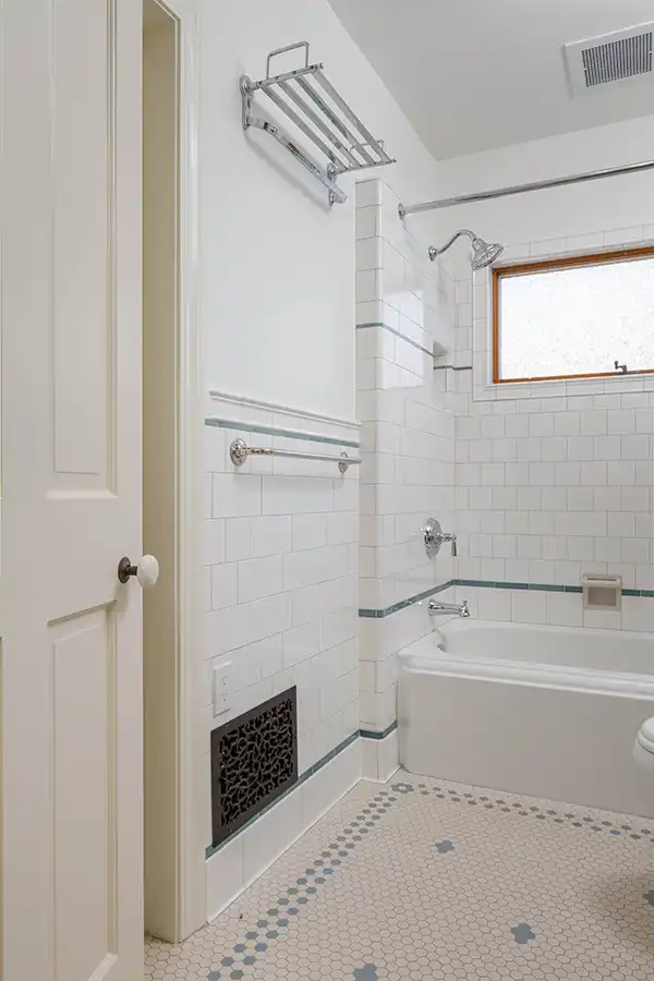 Tub and shower wall in white Subway Ceramics tile with blue-green liner, chrome towel rack, and a decorative cast iron heat register.