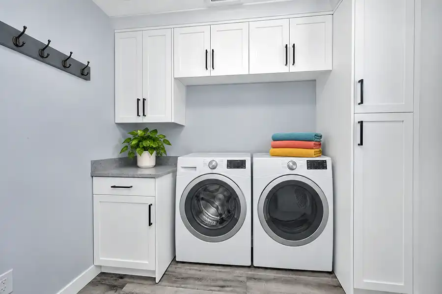 Laundry room with custom white Shaker cabinetry, tall storage cabinets, and a Piedrafina Pebble Beach countertop beside the washer space.