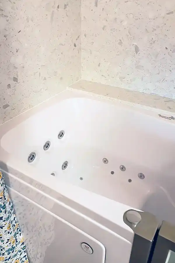 Jetted interior of the new walk-in tub, with the Piedrafina surround carried up the wall behind it.